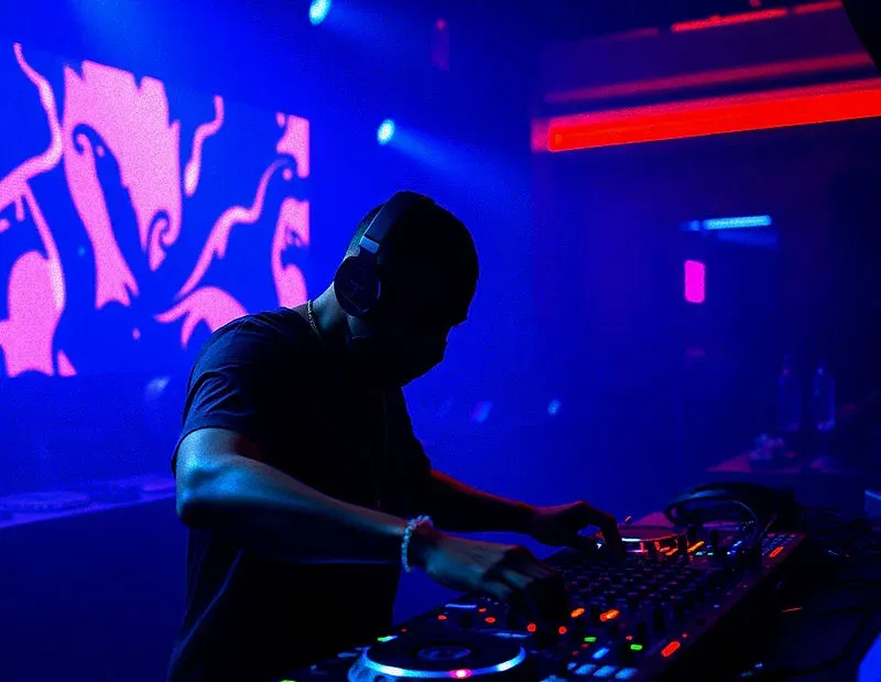 DJ performing beneath blue and magenta club lights